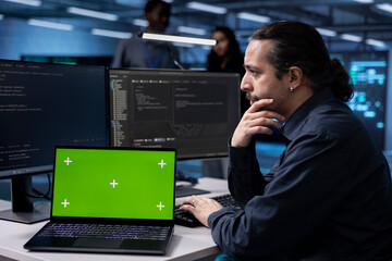 Man in server hub uses green screen laptop to find firewall misconfigurations affecting...