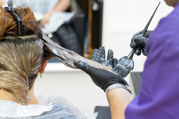 Hairdresser applying treatment to a client's hair in a beauty salon with a brush.