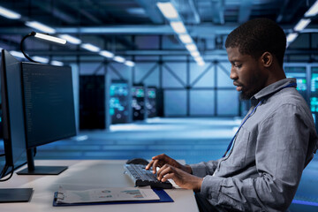 Employee checking for signs of imminent tech failure in data center supercomputers. African...