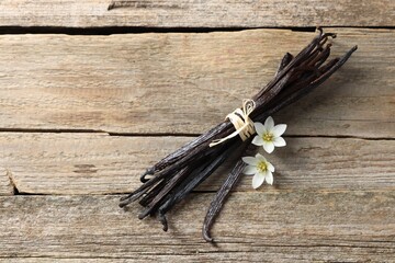 Bunch of vanilla pods and flowers on wooden table, top view. Space for text