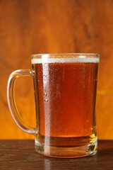 Mug with fresh beer on wooden table against color background