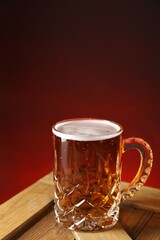 Mug with fresh beer on wooden crate against burgundy background