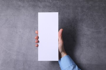 Woman holding blank card at grey table, top view. Mockup for design