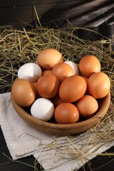 Fresh chicken eggs in bowl and dried hay on black wooden table
