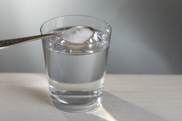 Spoon with baking soda over glass of water on table against light grey background, closeup. Space for text