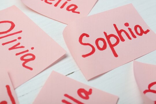 Paper stickers with different names on white wooden table, closeup. Choosing baby's name