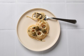Heart made of tasty spaghetti, fork, olives and cheese on white tiled table, top view