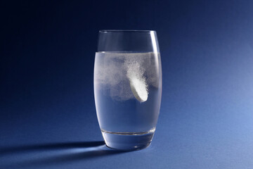 Effervescent pill dissolving in glass of water on blue background