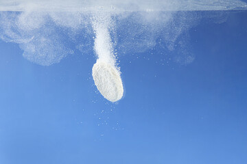Effervescent pill dissolving in water on blue background, closeup