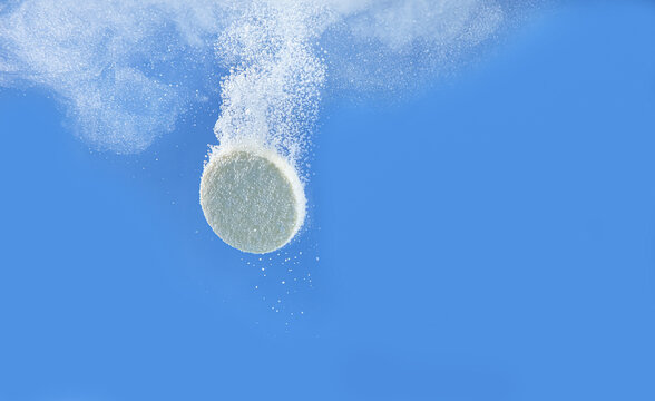 Effervescent pill dissolving in water on blue background, closeup