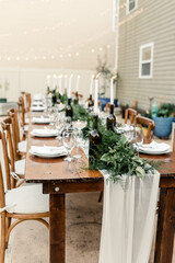 Elegant outdoor wedding table setting with greenery and candles

