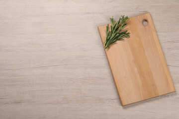 Cutting board and rosemary on light wooden table, top view. Space for text
