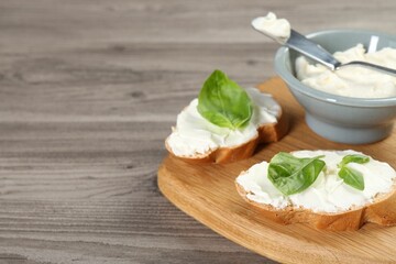Delicious sandwiches with cream cheese and basil leaves on wooden table, closeup. Space for text