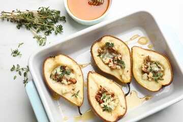 Tasty baked pears with nuts, blue cheese, thyme and honey in baking dish on table, flat lay