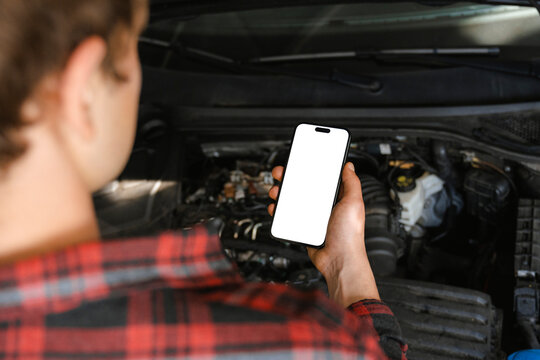 A man uses a mobile phone with white screen in a car repair shop