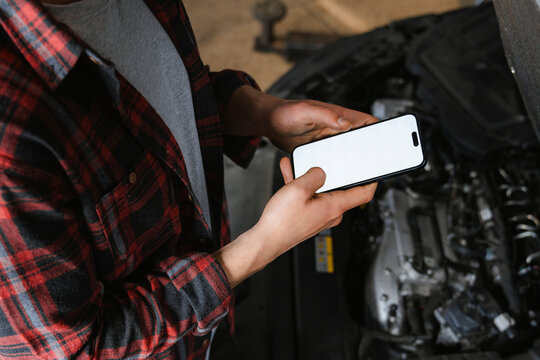 A man uses a mobile phone with white screen in a car repair shop