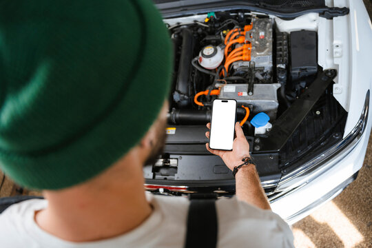 A man uses a mobile phone with white screen in a car repair shop