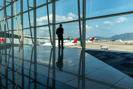 A man standing alone inside an airport looking out.