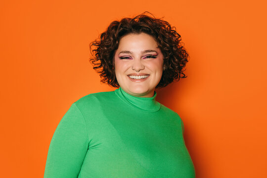 Joyful curvy woman in green sweater against orange background