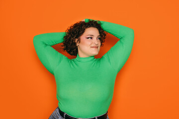 Joyful curvy woman in green top on orange background
