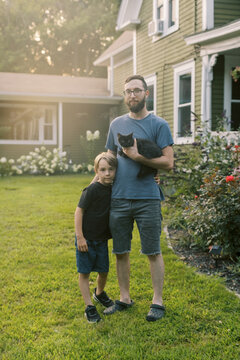father and son holding black kitten while standing in front of home
