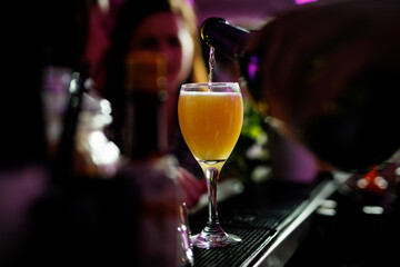 The Bartender pours a golden, effervescent beverage into an elegant glass