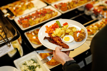 Guest picks up different food at breakfast buffet at hotel.