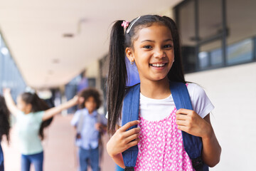 Biracial girl with backpack smiling at school