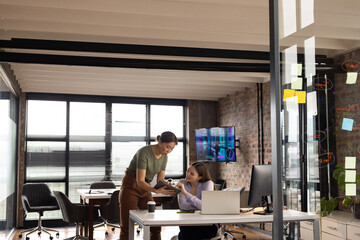 Asian businesswoman showing something on tablet to young Caucasian woman in modern office