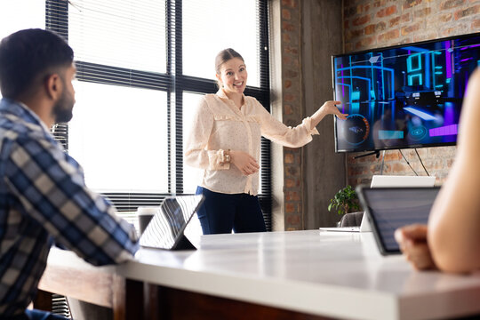 Asian businesswoman presenting data on screen to a diverse team in office