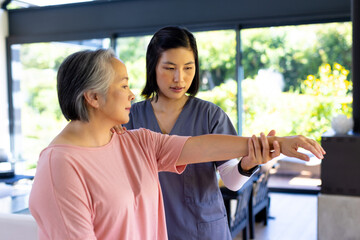 Physical therapist healthcare worker assisting senior Asian woman with arm exercises