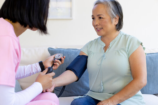 Asian senior woman having blood pressure checked by Asian nurse healthcare worker