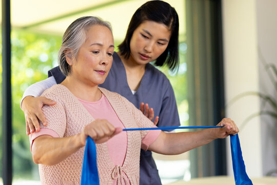 Asian senior woman exercises with resistance band, aided by Asian physical therapist