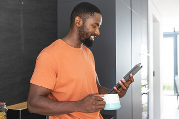 Young African American man holding tablet and a coffee mug, smiling at screen