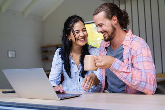 Young diverse couple are smiling while looking at a laptop - Powered by Adobe