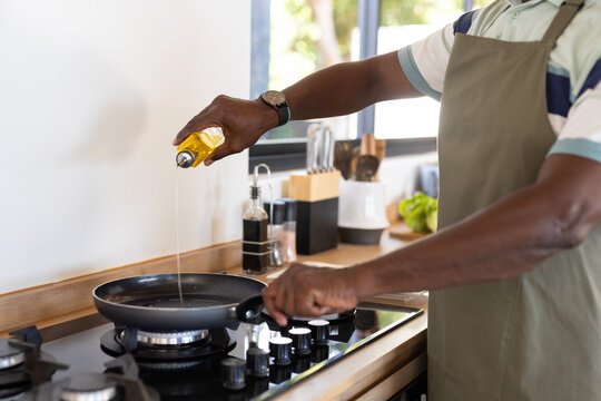 African American mature man cooking in kitchen, pouring oil into frying pan