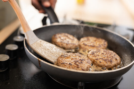 Four burgers frying in a pan, close up