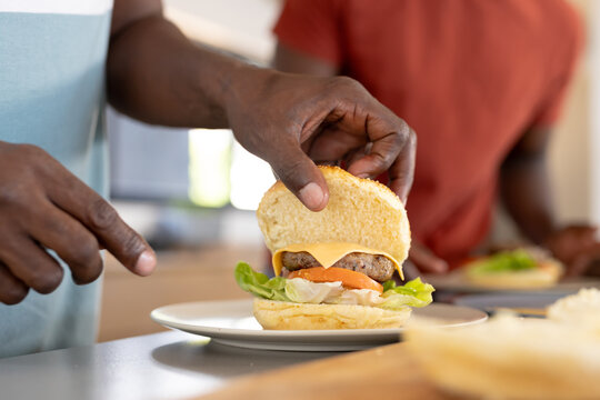 African American father and son preparing cheeseburger together in kitchen