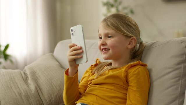 Happy little girl sofa holding mobile phone smartphone rejoice good news winning victory excited enjoy child kid successful celebrate joyful technology yes luck gadget home delighted female cellphone