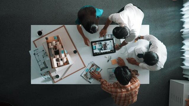 Time lapse of designer looking at model while discussing about building. Top view of architect engineer explaining idea while talking and writing blue print scattering at meeting table. Alimentation.