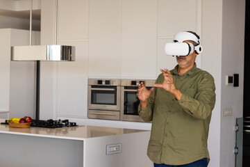 Mature biracial man wearing VR headset, interacting with virtual objects, at home, copy space