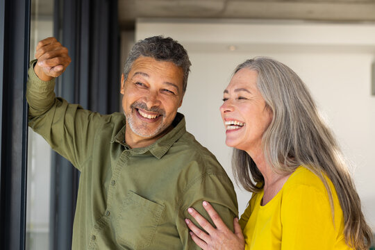 A biracial mature couple, mature Caucasian woman and a mature man, smiling together, at home