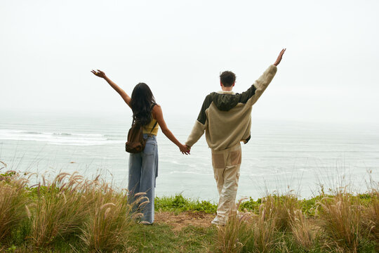 Pareja de novios sujetados de la mano mirando el paisaje  frente al mar