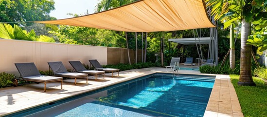 Swimming pool surrounded by a fence in the garden, complemented by sunbeds under a stylish shade sail