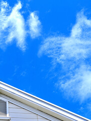 A clear blue sky with white clouds and a white roof on a house.
