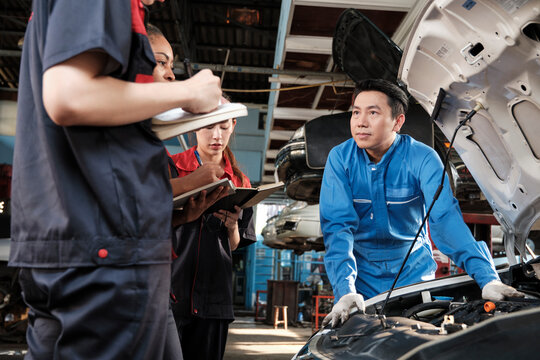 Asian male professional automotive engineer supervisor describes car engine maintenance and repair work with mechanic worker staffs team in fix service garage, specialist occupations in auto industry.