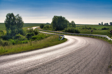 Empty, curved road stretches through a rural landscape under a clear blue sky