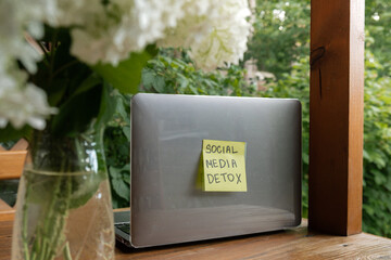 SOCIAL MEDIA DETOX text on paper note at laptop on background of greenery garden wooden alcove...