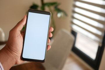 A hand holds a smartphone in a modern home interior, highlighting technology and lifestyles