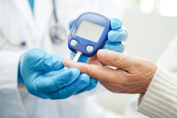 Asian doctor using digital glucose meter for check sample blood sugar level to treatment diabetes.